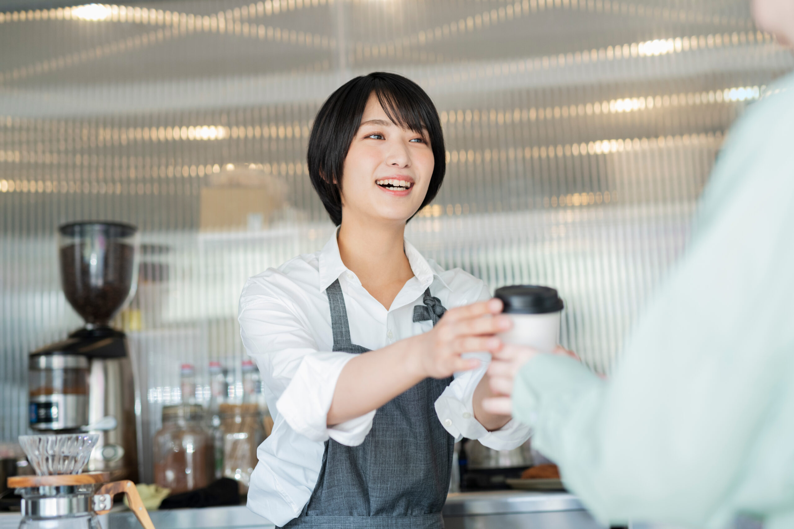 カフェスタッフがテイクアウトのコーヒーを手渡す様子